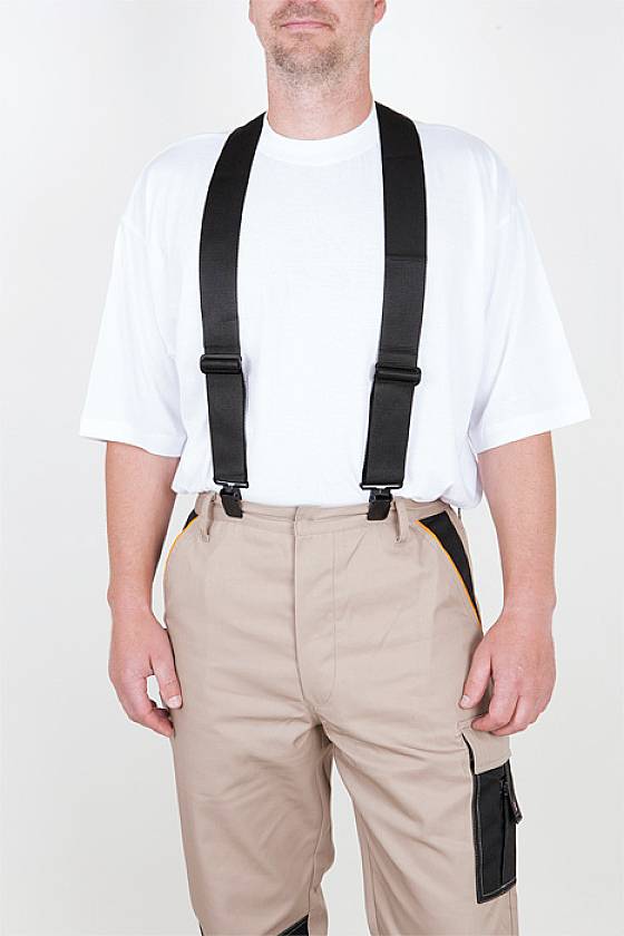 Ein Mann trägt ein weißes T-Shirt, beige Arbeitshose und schwarze Hosenträger.