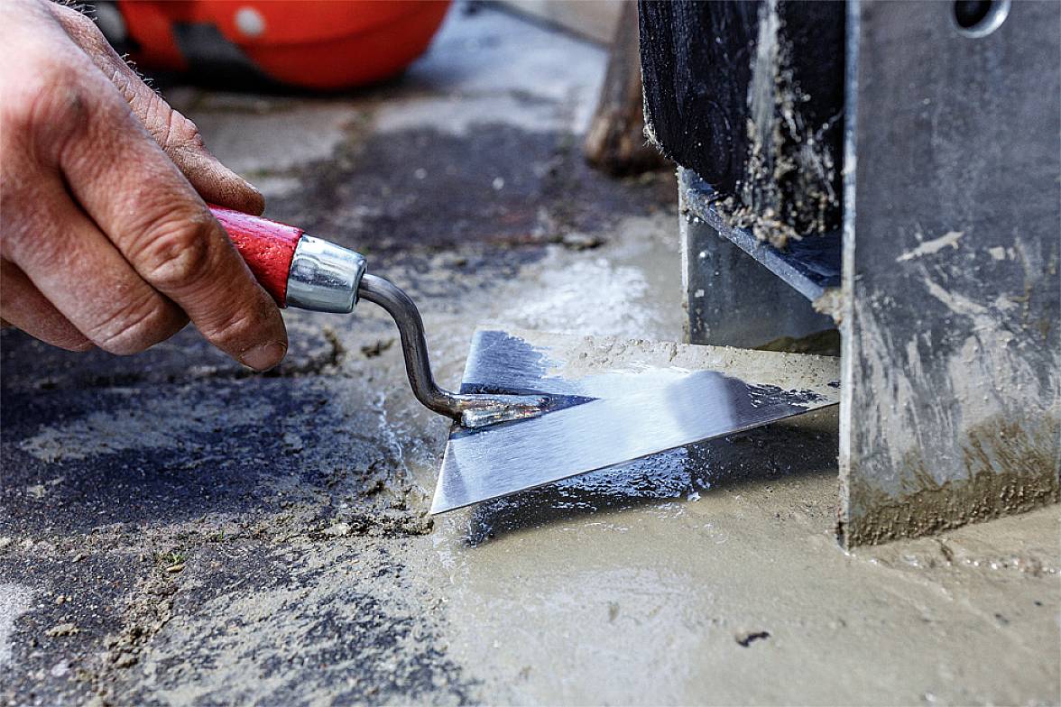 'Arbeiter glättet frischen Zement mit einer Kelle auf einer Baustelle, Detailaufnahme der Hand in Aktion.'