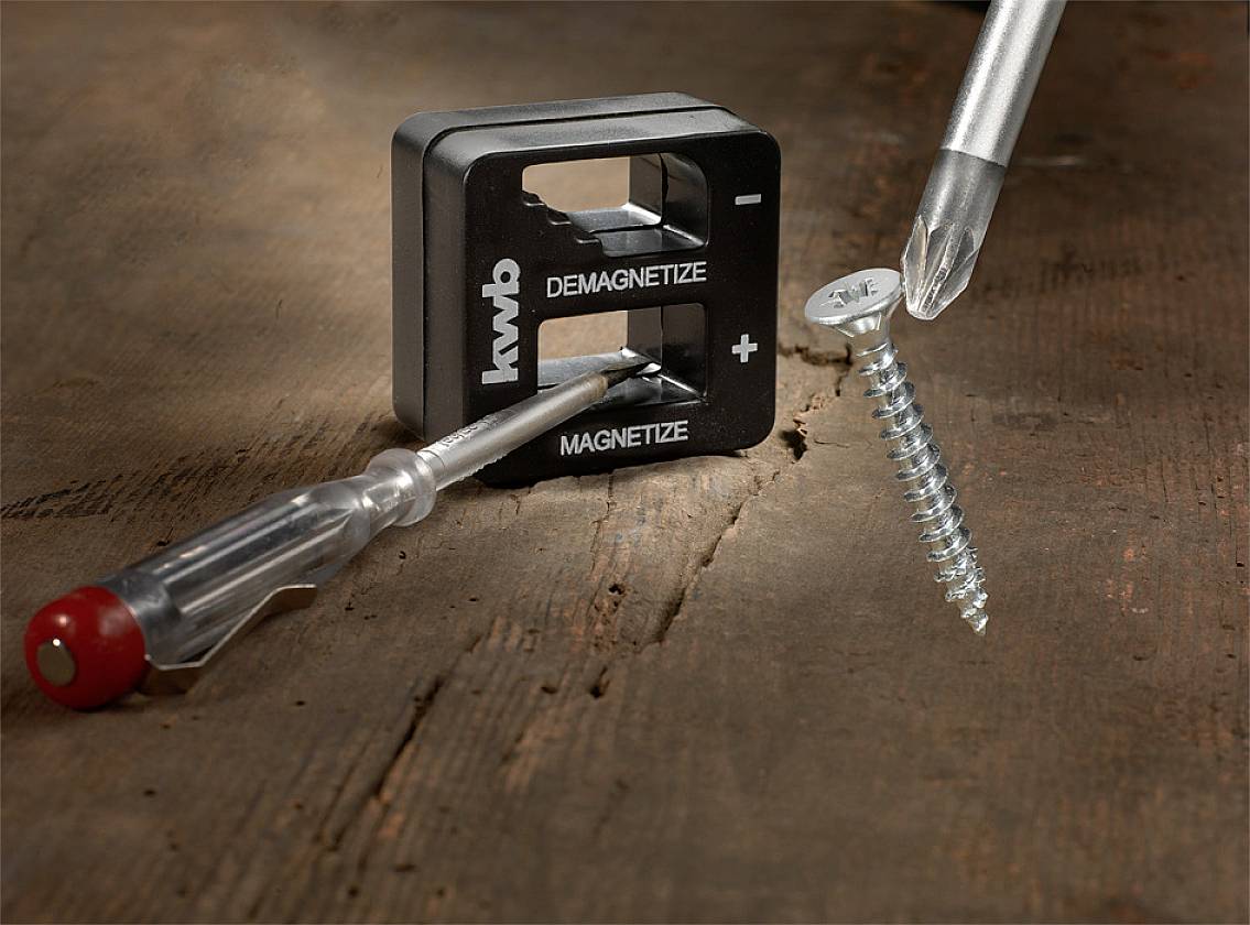 Ein Schraubenzieher neben einem Magnetisierer auf Holzoberfläche, mit einer Schraube, die von einem weiteren Schraubenzieher gehalten wird.
