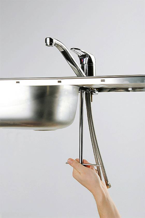 Eine Hand befestigt ein Installationswerkzeug an einem Wasserhahn unter einem Waschbecken.