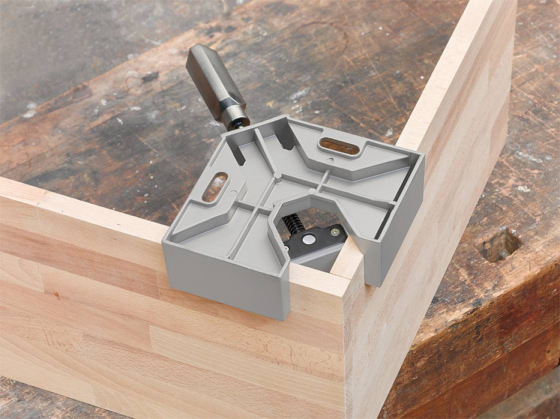 Ein grauer Gehrungswinkel liegt auf einer hellen Holzplatte, um präzise 90-Grad-Winkel beim Zuschneiden zu unterstützen.