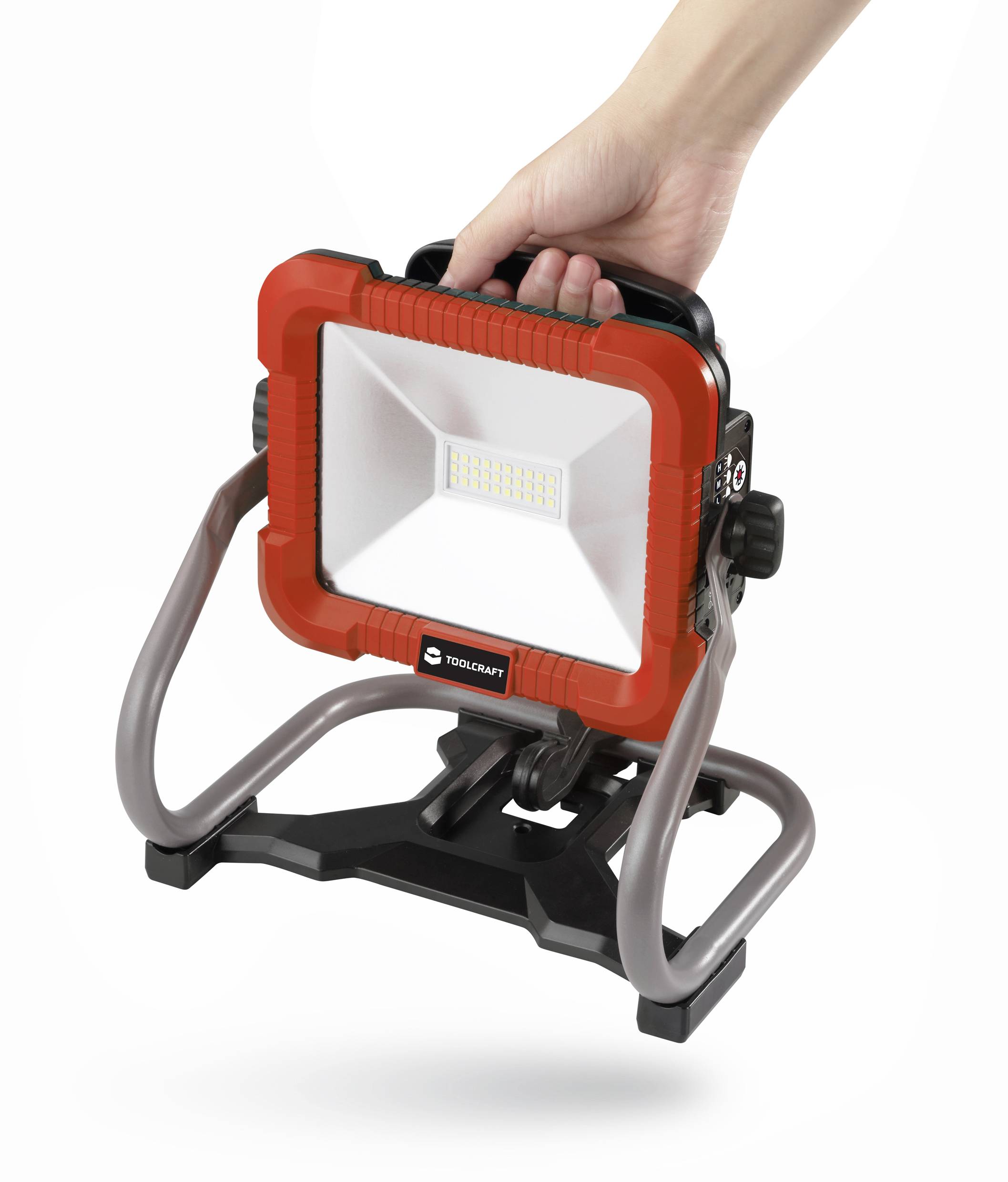 Eine Hand hält einen tragbaren, rot-schwarzen LED-Baustrahler mit einem stabilen Ständer, geeignet für den Einsatz auf Baustellen.