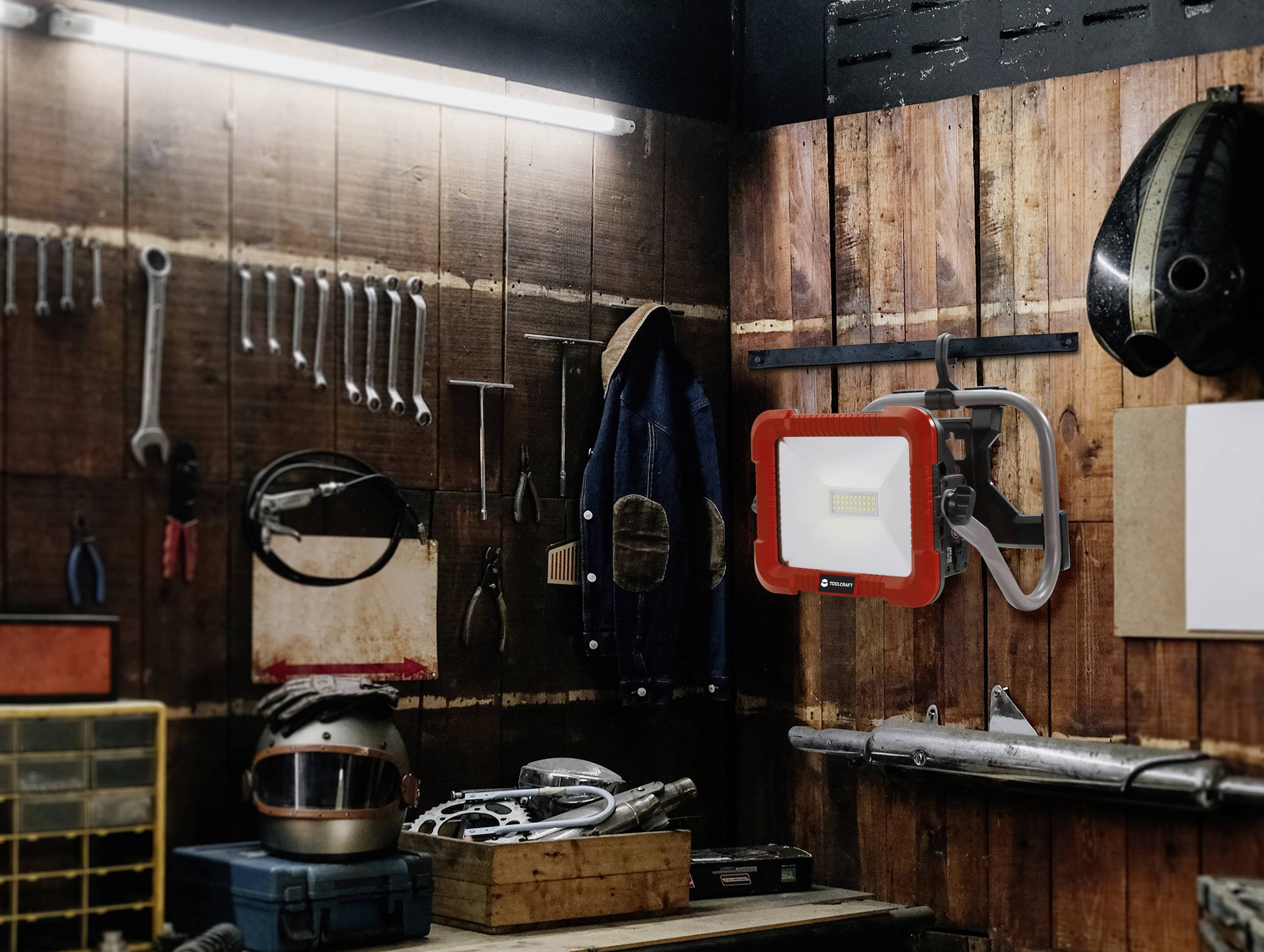 Eine Werkstatt mit Werkzeugen an Holzwänden: Schraubenschlüssel, Schraubenzieher und ein Arbeitslicht. Ein Helm und Maschinenteile auf dem Tisch.