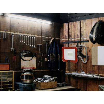 Eine Werkstatt mit Werkzeugen an Holzwänden: Schraubenschlüssel, Schraubenzieher und ein Arbeitslicht. Ein Helm und Maschinenteile auf dem Tisch.