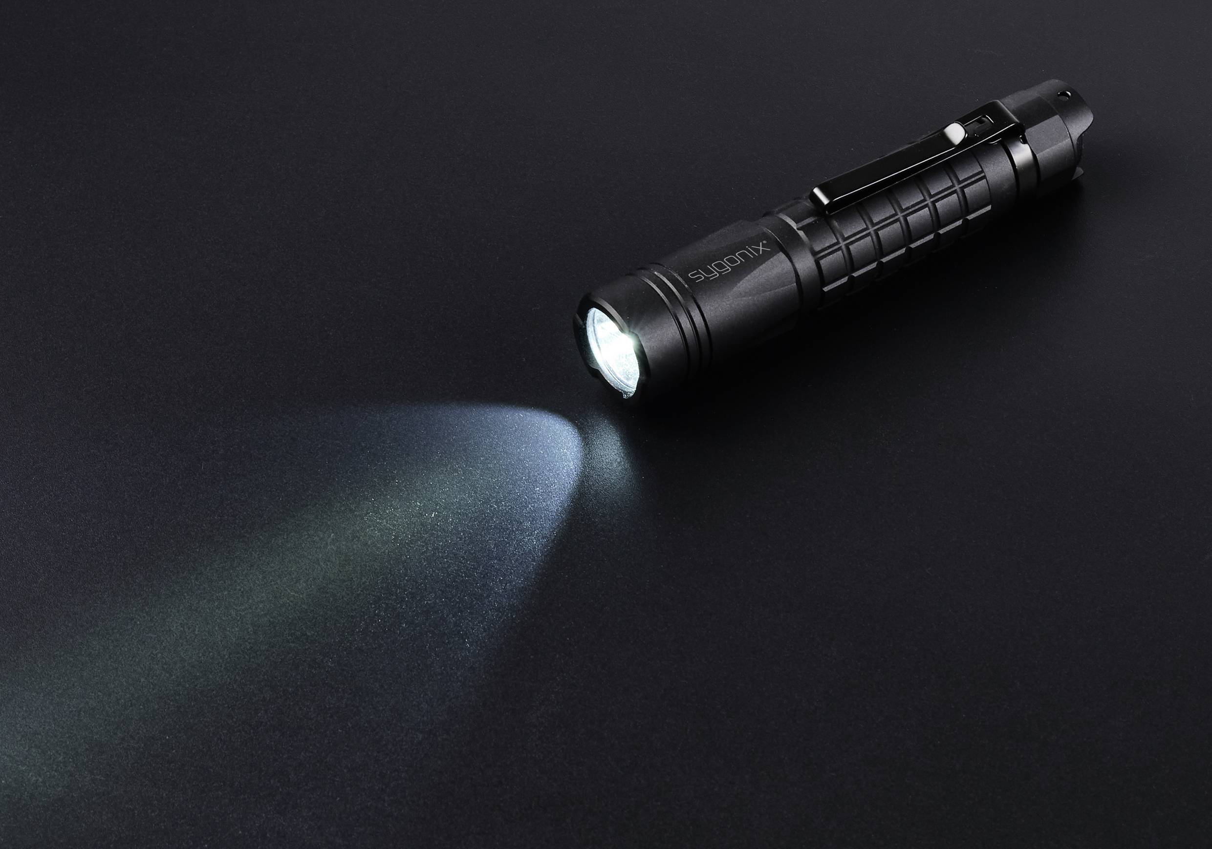 Schwarze Taschenlampe strahlt helles Licht auf dunkle Oberfläche.