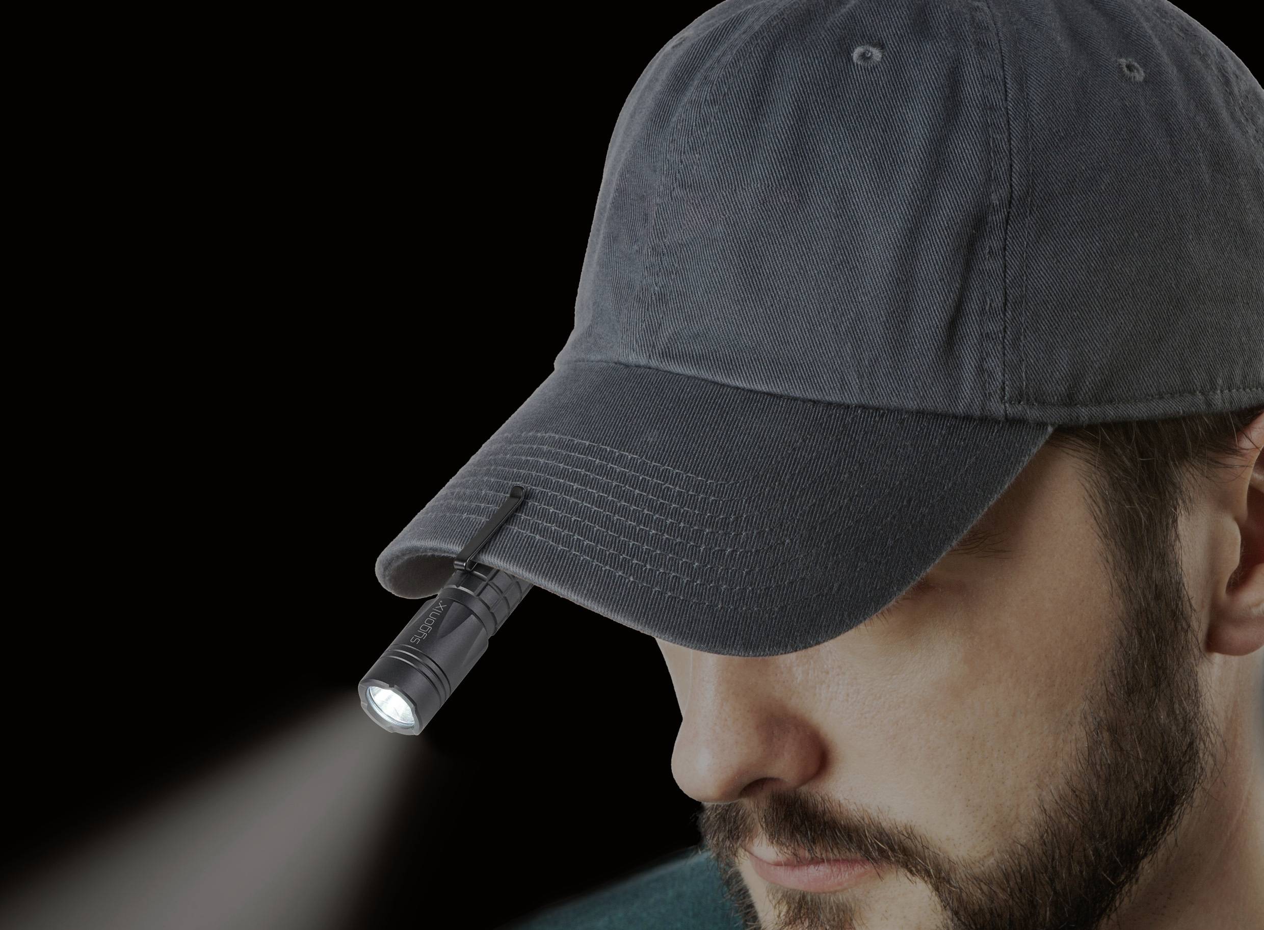 Ein Mann mit einem dunklen Basecap, an dem eine kleine Taschenlampe befestigt ist, die nach vorne leuchtet.