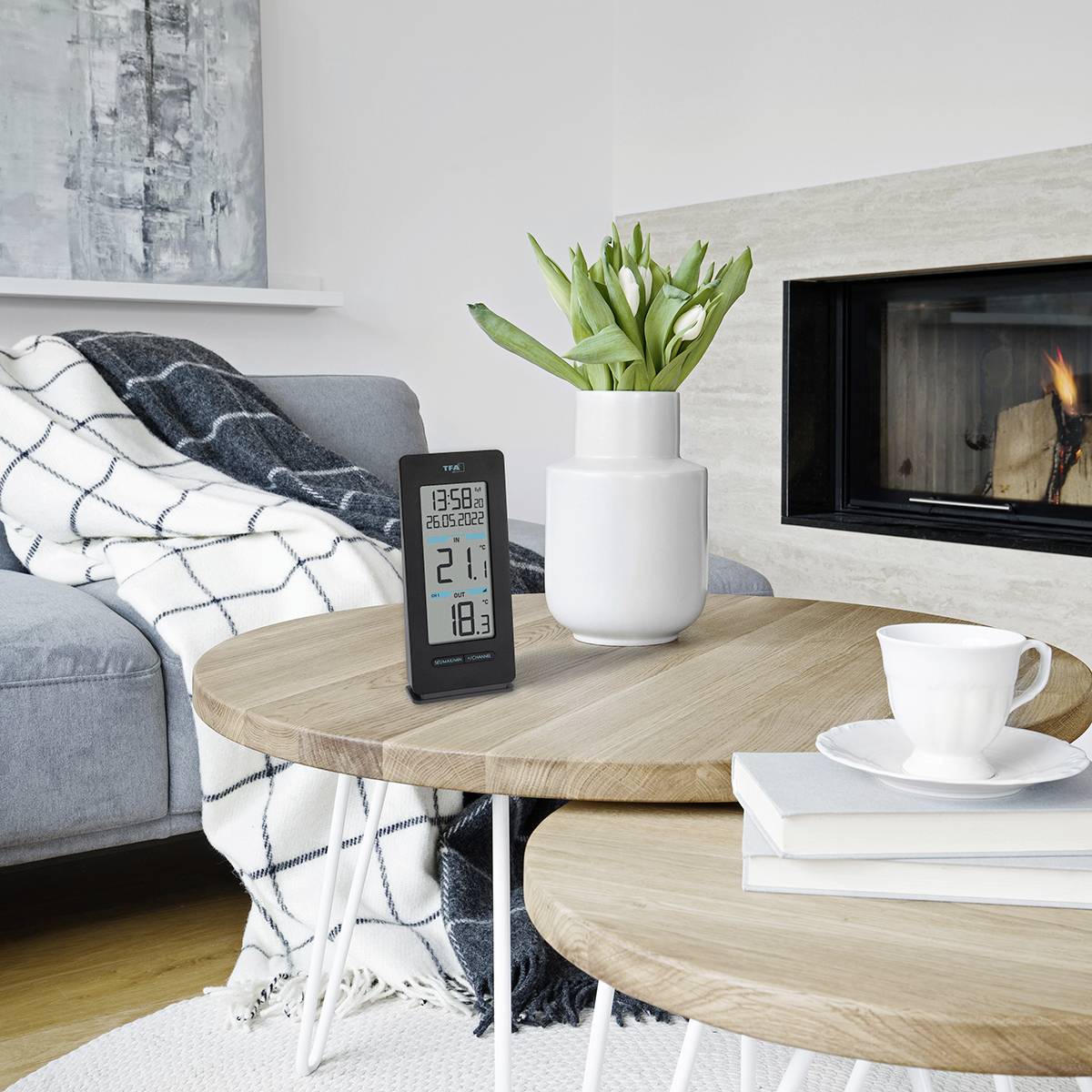 Ein Wohnzimmer mit einem Sofa, ein Thermometer zeigt 23 Grad. Ein Blumentopf auf dem Tisch, ein Kamin im Hintergrund.