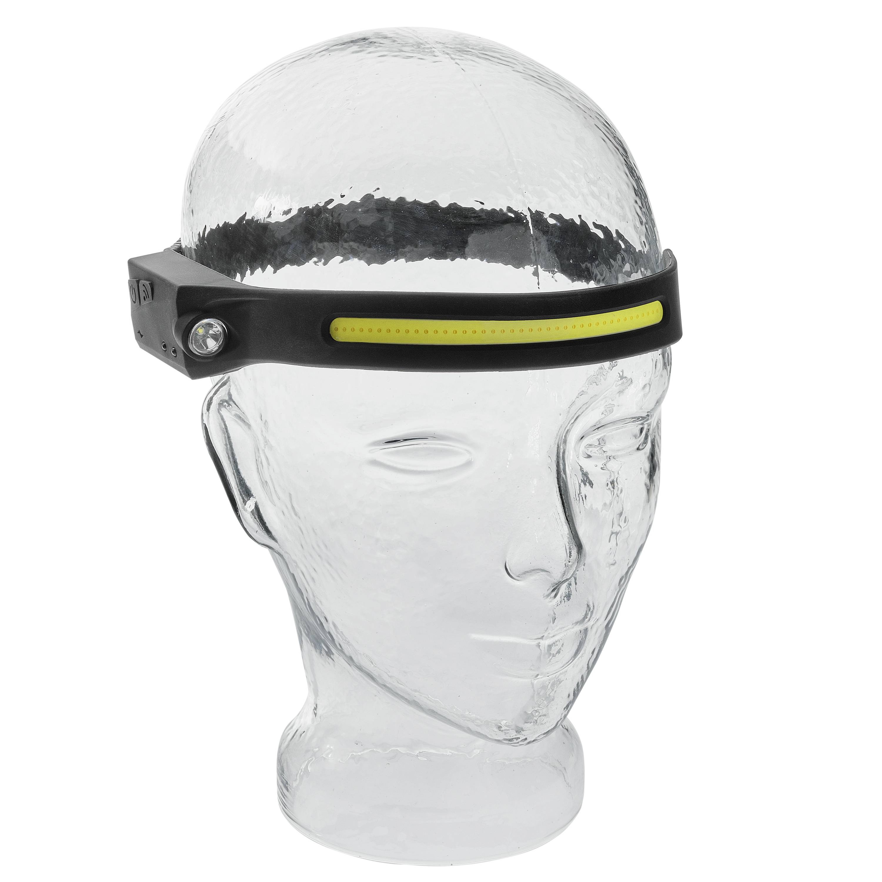 Durchsichtiger Glas-Kopf zeigt eine schwarze Stirnlampe mit gelbem LED-Streifen und seitlichem Knopf.
