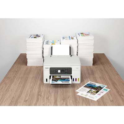 Ein Drucker auf einem Tisch druckt ein farbiges Foto. Im Hintergrund befinden sich stapelweise bedruckte Papiere.