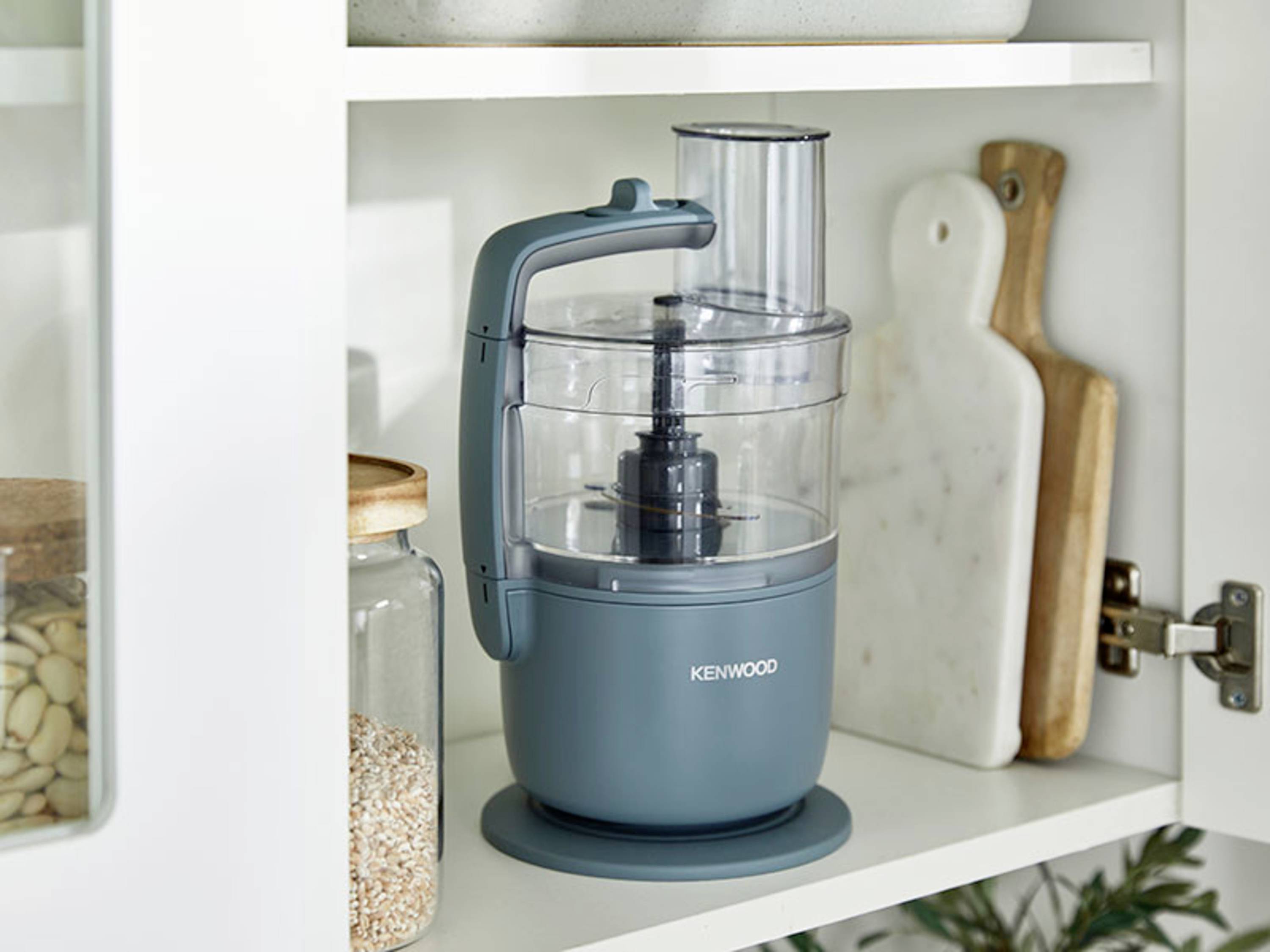 Ein blauer Küchenmixer steht in einem weißen Schrank, umgeben von Gläsern mit Lebensmitteln und Schneidebrettern.