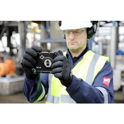 Ein Arbeiter in Schutzkleidung und Helm hält ein Messgerät in der Hand, konzentriert bei der Arbeit in einer industriellen Umgebung.