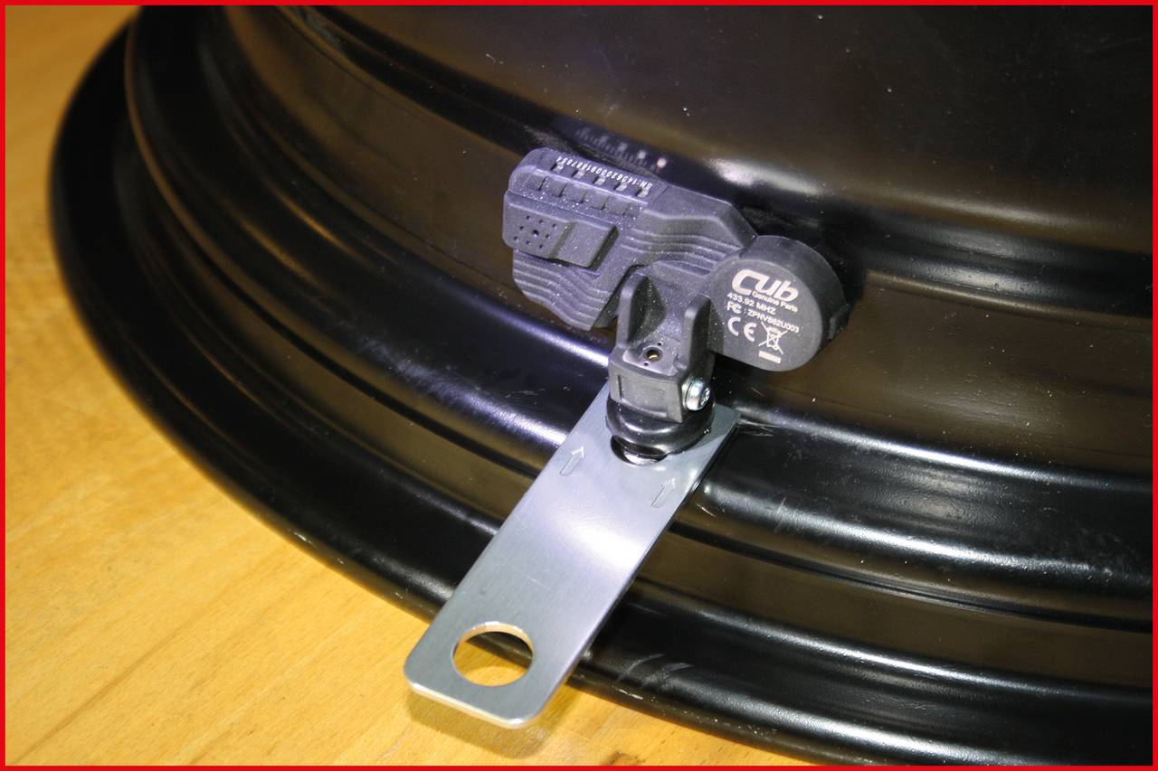'Ein Reifendrucksensor ist an einem Fahrzeugrad montiert, er zeigt Details der Halterung und des Sensors auf einer Metallfelge.'