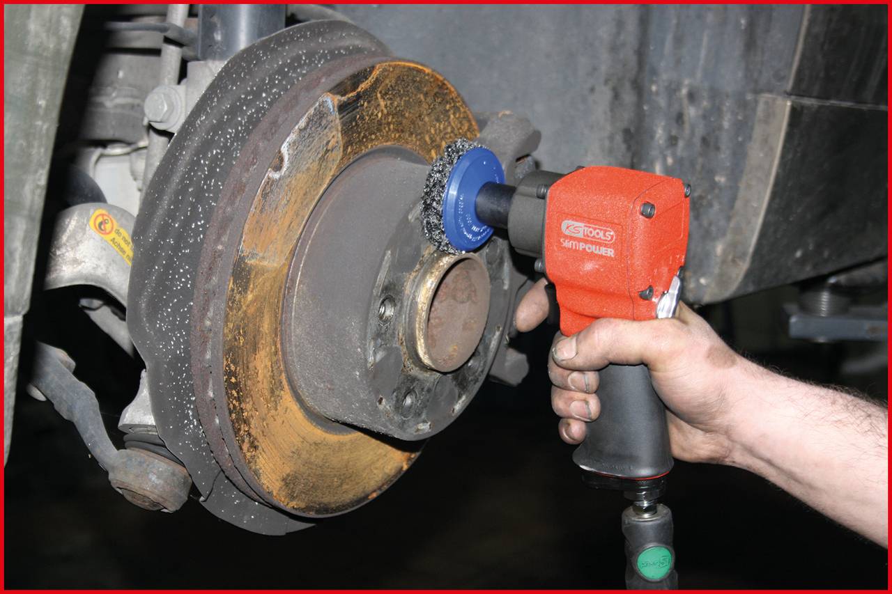'Nahaufnahme einer Hand, die mit einem elektrischen Werkzeug Rost von einer Bremsscheibe an einem Fahrzeug entfernt.'