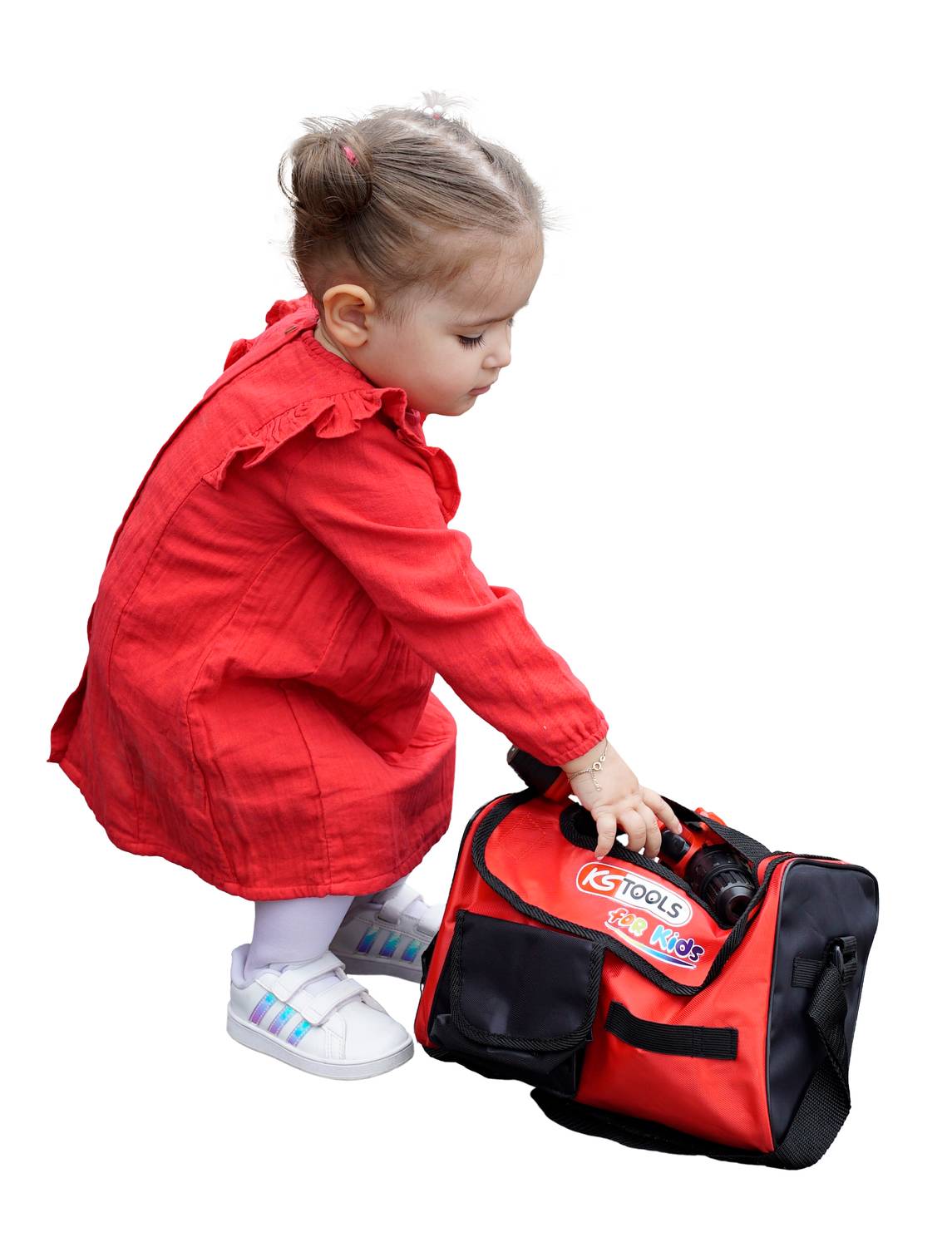 Kleines Kind in rotem Kleid beugt sich vor und hält eine Tasche mit Werkzeugen, als ob es etwas herausnehmen möchte.