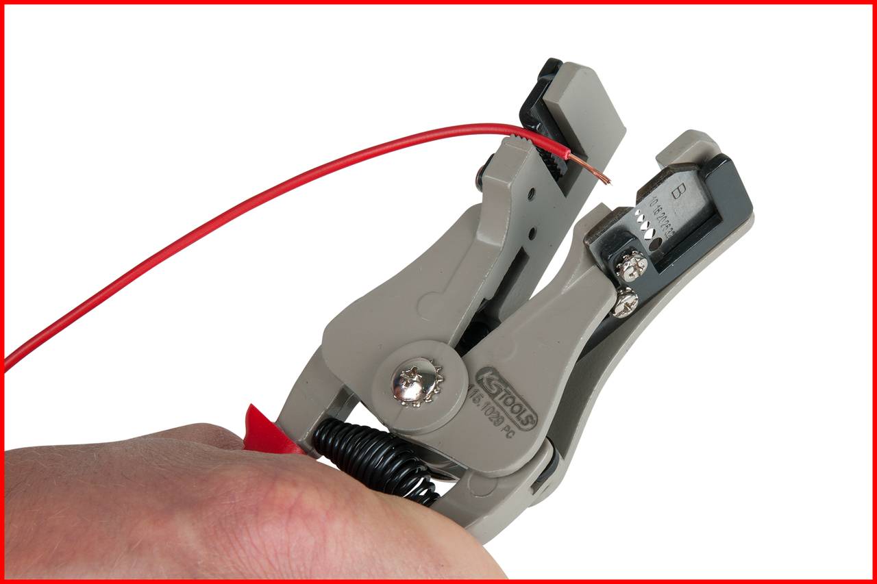 Eine Hand hält eine Abisolierzange, die ein rotes Kabel abisoliert.