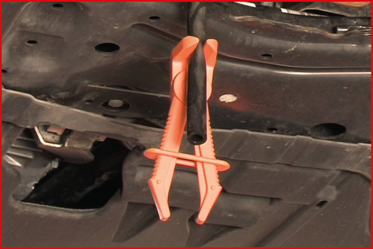 Eine orangefarbene Klammer hält einen schwarzen Schlauch unter der Motorhaube eines Fahrzeugs fest.
