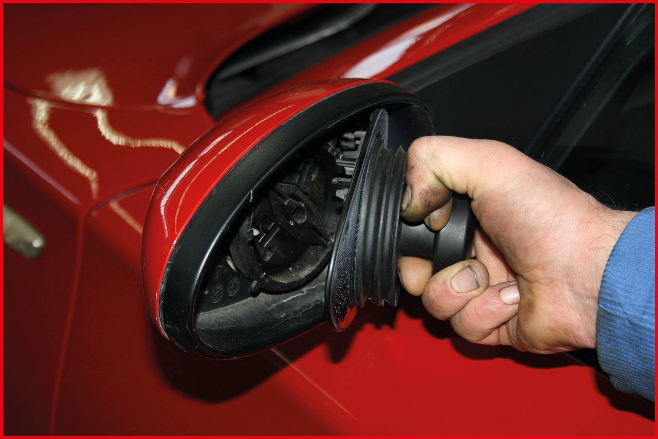 Ein beschädigter roter Autoaußenspiegel wird von einer Hand gehalten. Der Spiegel ist abgebrochen und zeigt innere Mechanik.