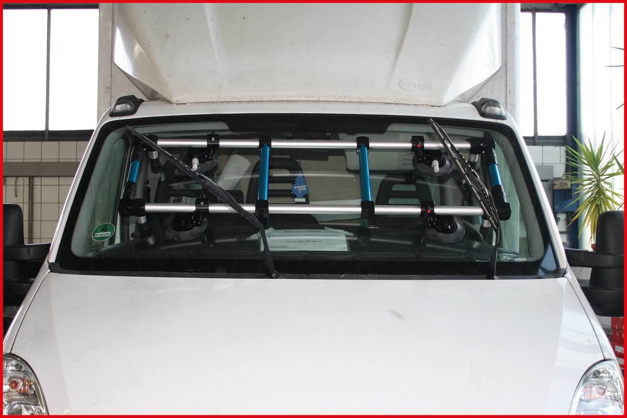 Ein weißer Transporter mit einer an der Windschutzscheibe montierten Aluminiumleiter in einer Werkstatt.