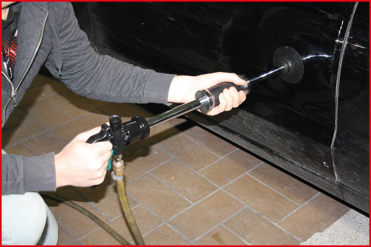 'Person poliert ein Auto mit einer elektrischen Poliermaschine auf einem braunen Fliesenboden.'