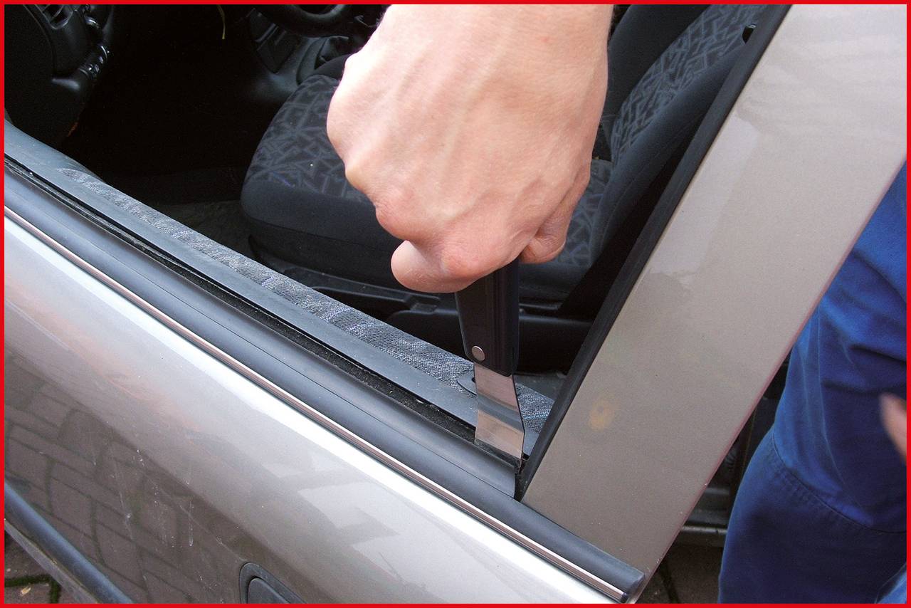 Ein Blick auf eine Person, die mit einem Messer einen Autotürrahmen manipuliert, möglicherweise ein Einbruch oder Vandalismus.