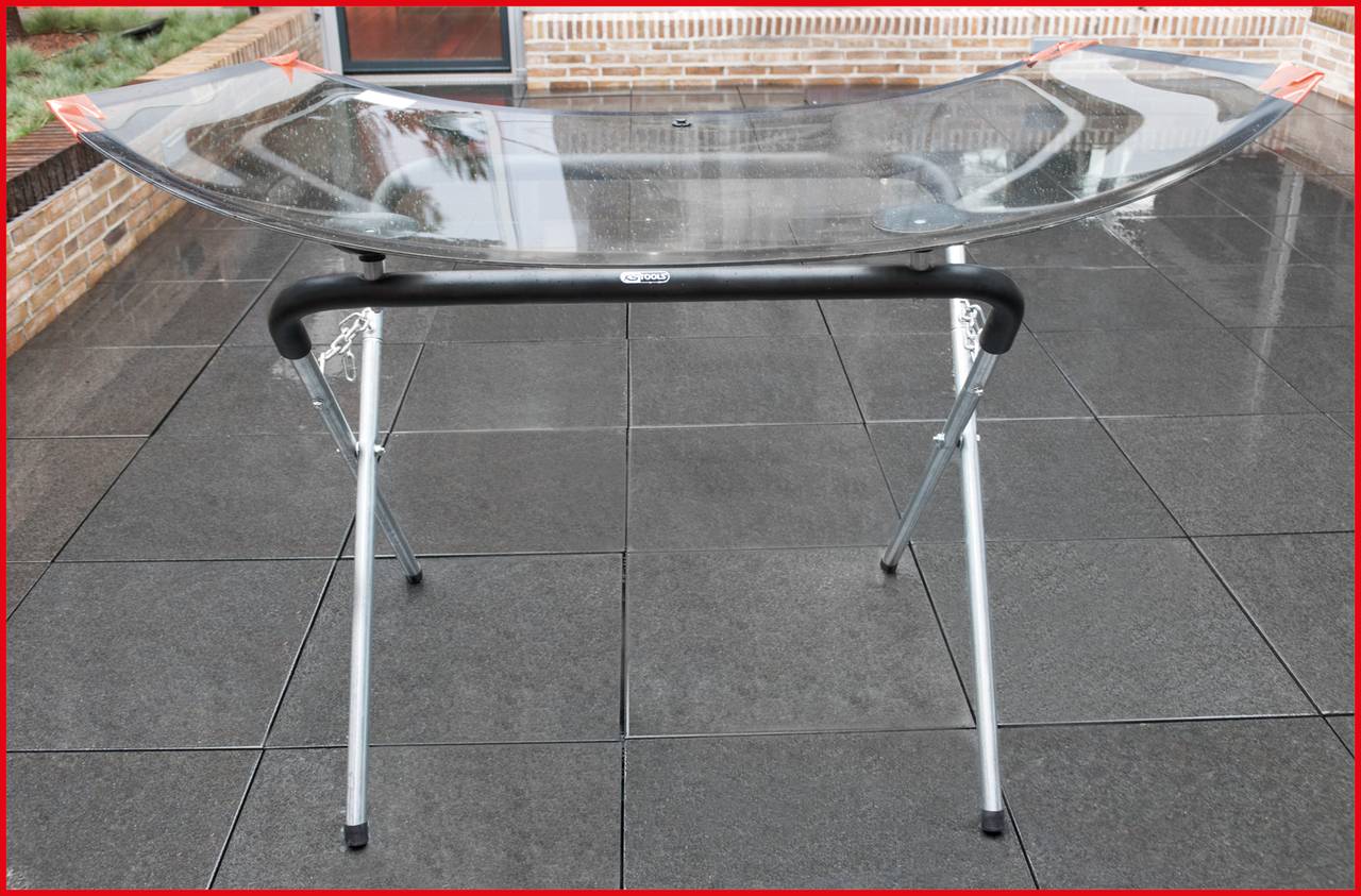 Ein transparentes Designelement wird auf einem Metallgestell im Freien präsentiert. Der Boden ist mit großen, dunklen Fliesen bedeckt.