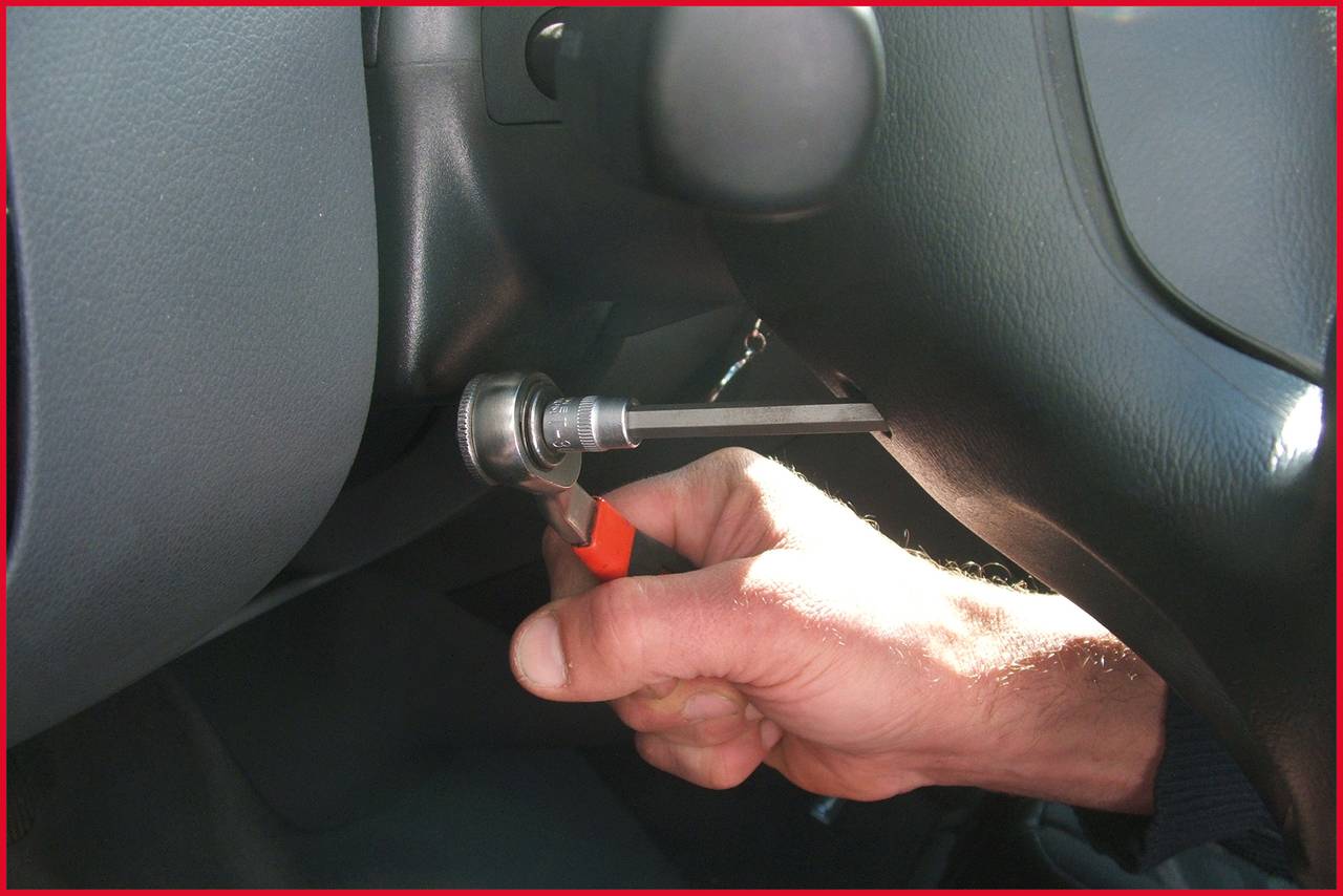 Eine Hand hält ein Schraubendreher-Werkzeug in einem Zündschloss eines Autos, was auf eine mögliche Manipulation hinweist.