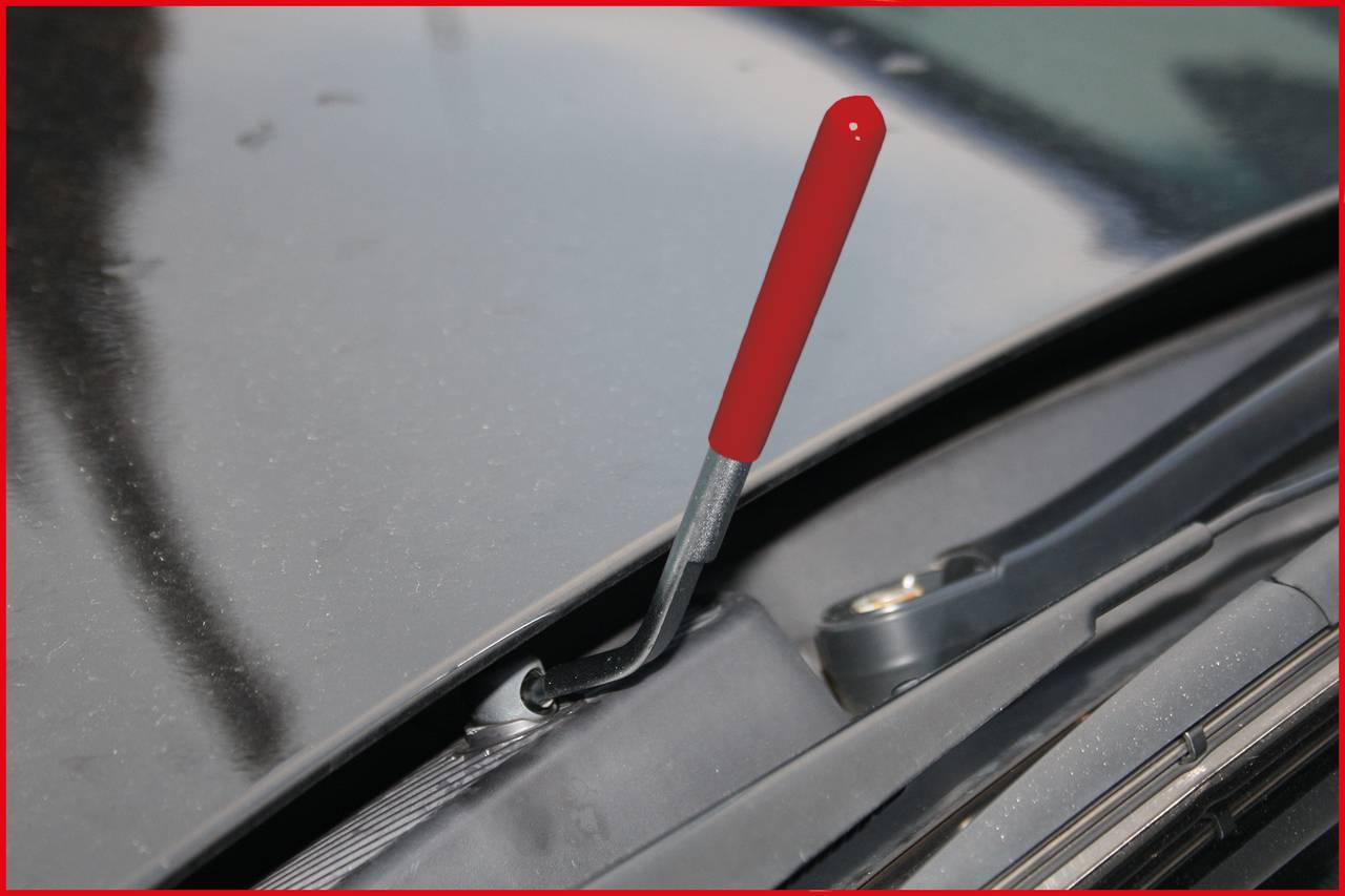 'Ein Hebel mit rotem Griff ragt aus einer Motorhaube eines Autos, nahe einem Scheibenwischer.'