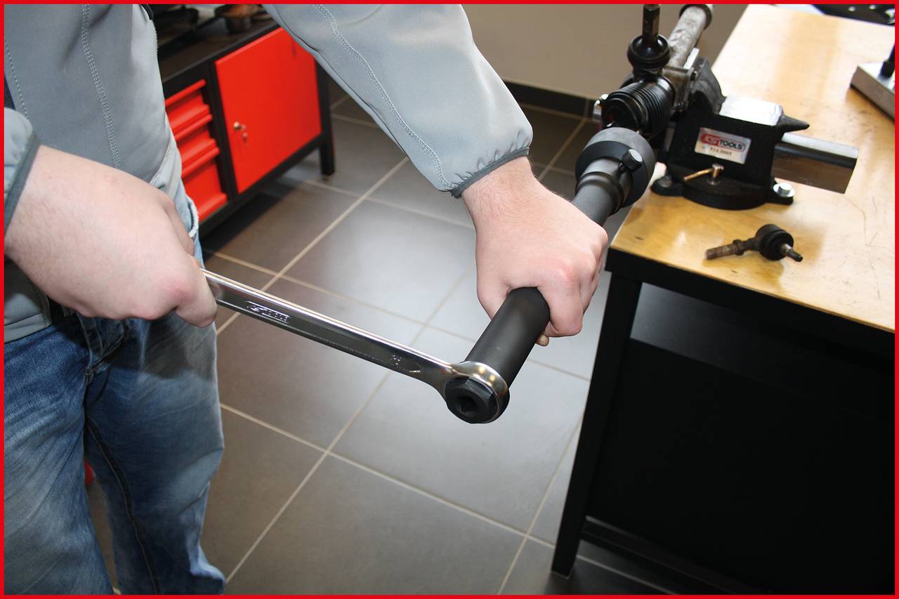 Eine Person verwendet einen Drehmomentschlüssel, um ein Bauteil in einer Werkstatt zu reparieren. Im Hintergrund sind Werkbänke sichtbar.