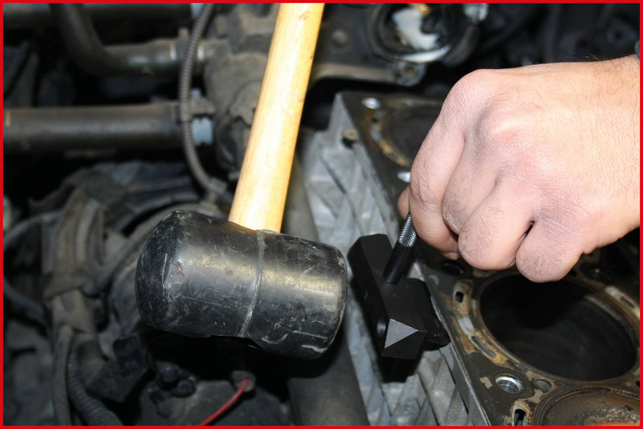 Ein Mensch nutzt Hammer und Werkzeug, um an einem Motorblock zu arbeiten. Fokus liegt auf der Hand und dem Werkzeug.