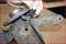 Eine Hand hält einen Sensor, der an einem rostigen Autoteil befestigt ist. Das Bild zeigt die Reparatur oder Überprüfung eines Fahrzeugteils.