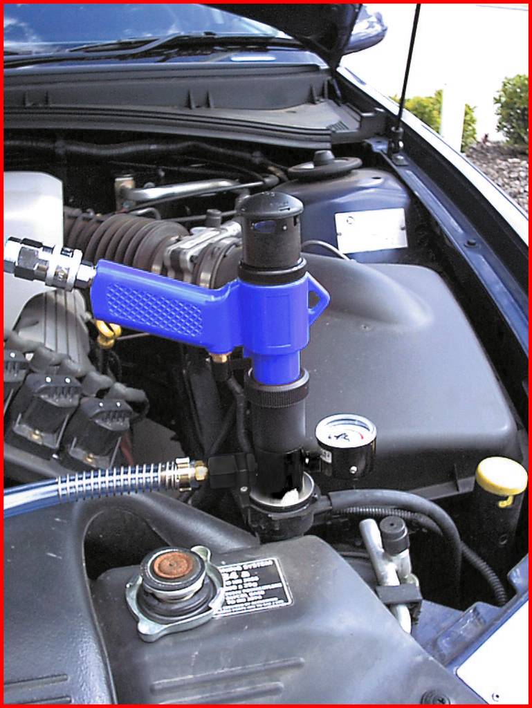 Ein blauer Werkzeugaufsatz wird an einem Auto-Motorteil befestigt, vermutlich für eine Wartung oder Reparatur, mit offenem Motorraum.