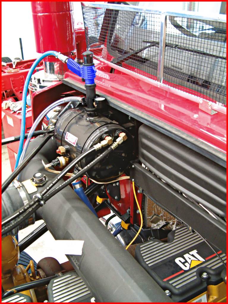 'Nahaufnahme eines Motorraums mit verschiedenen Teilen, Rohren und Kabeln in einem Fahrzeug. Hauptsächlich Maschinenkomponenten sichtbar.'