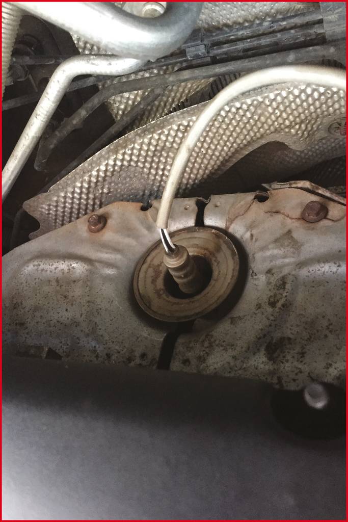 Ein Abgasrohr mit einem Sensor, der an einem Kabel befestigt ist, sichtbar im Motorraum eines Fahrzeugs.