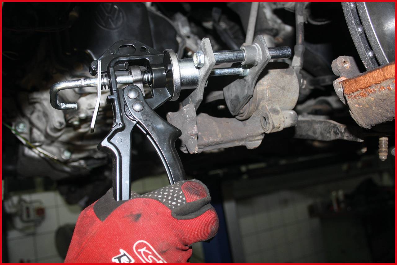 Eine behandschuhte Hand hält ein Werkzeug, um an einem Autoteil zu arbeiten. Es scheint sich um eine Reparatur oder Wartungsarbeit zu handeln.
