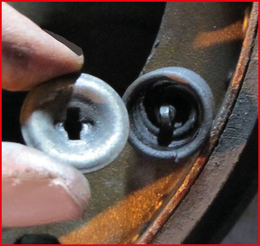 Nahaufnahme eines kaputten Metallschlosses mit einem passenden Schließzylinder, der von einer Hand gehalten wird.