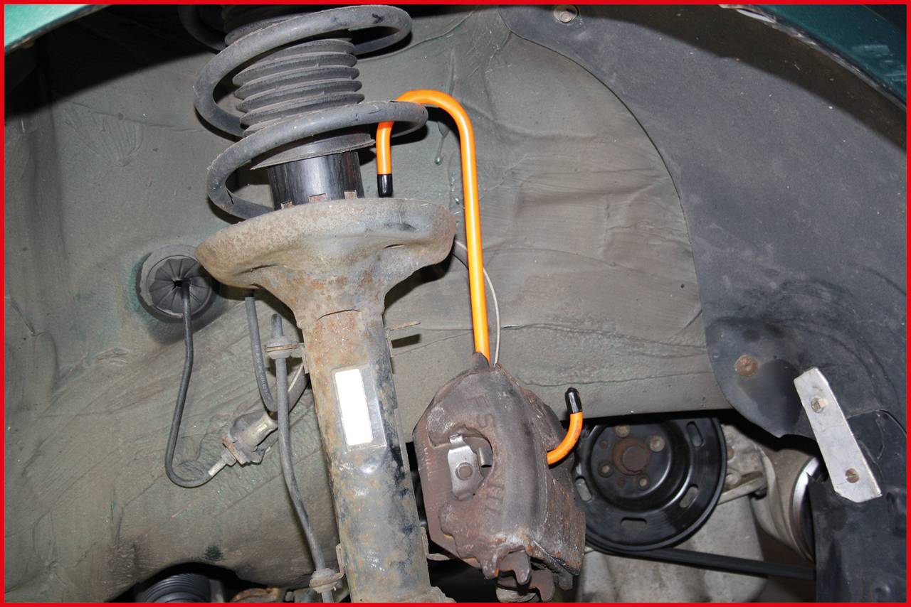 Das Bild zeigt eine Nahaufnahme eines Fahrwerks mit Stoßdämpfer und Bremsklotz eines Fahrzeugs. Deutliche Abnutzung und Kabel sind sichtbar.