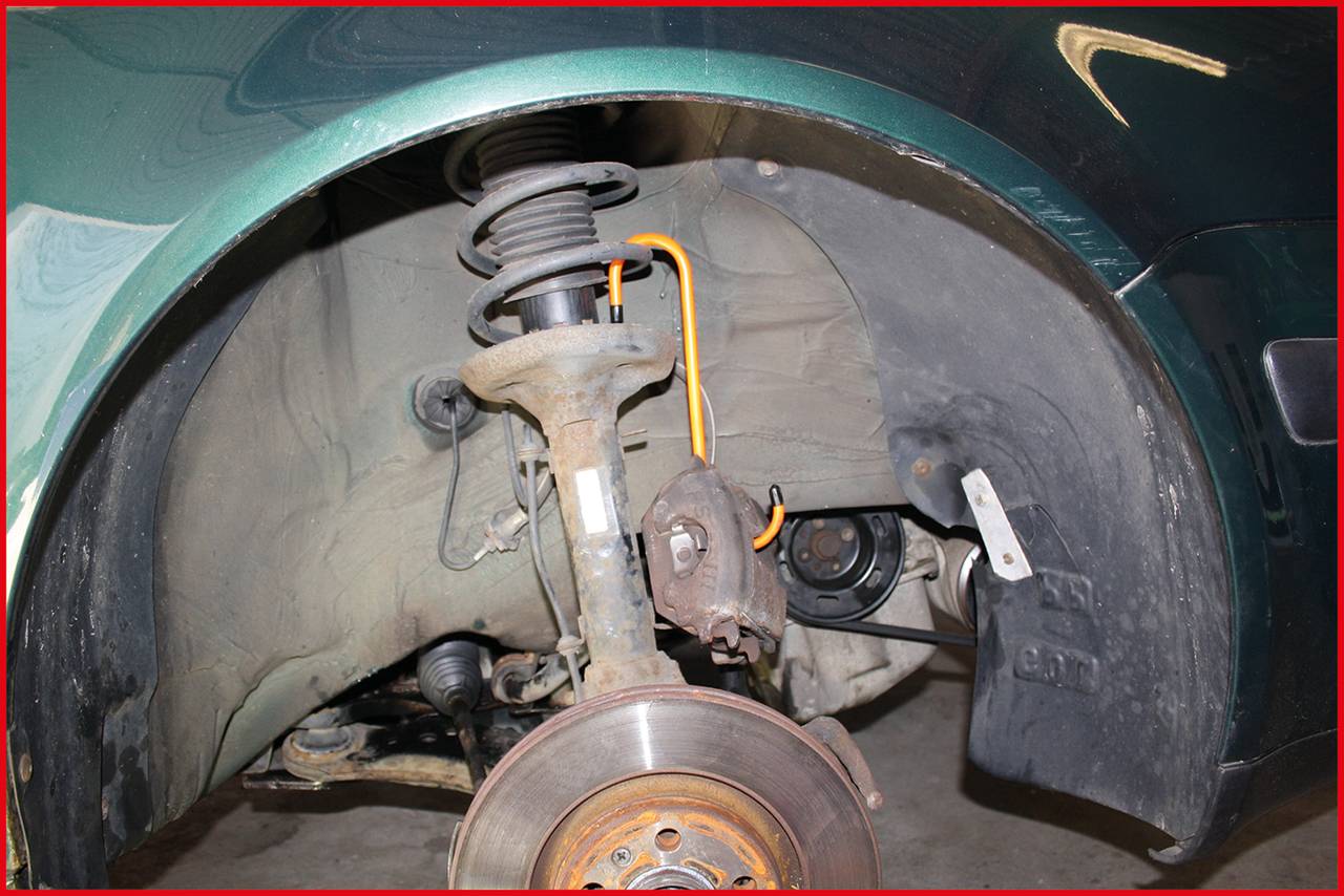 Ein Auto, dessen Rad entfernt wurde, zeigt das Fahrwerk und die Bremsanlage. Sichtbar sind Federbein, Bremsscheibe und Bremsbeläge.