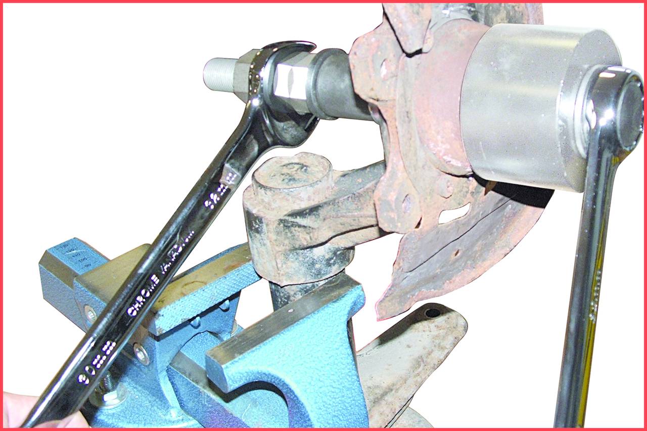 Zwei Schraubenschlüssel ziehen eine Mutter an einer rostigen Metallverbindung in einem Schraubstock an, für Reparaturen oder Montagearbeiten.