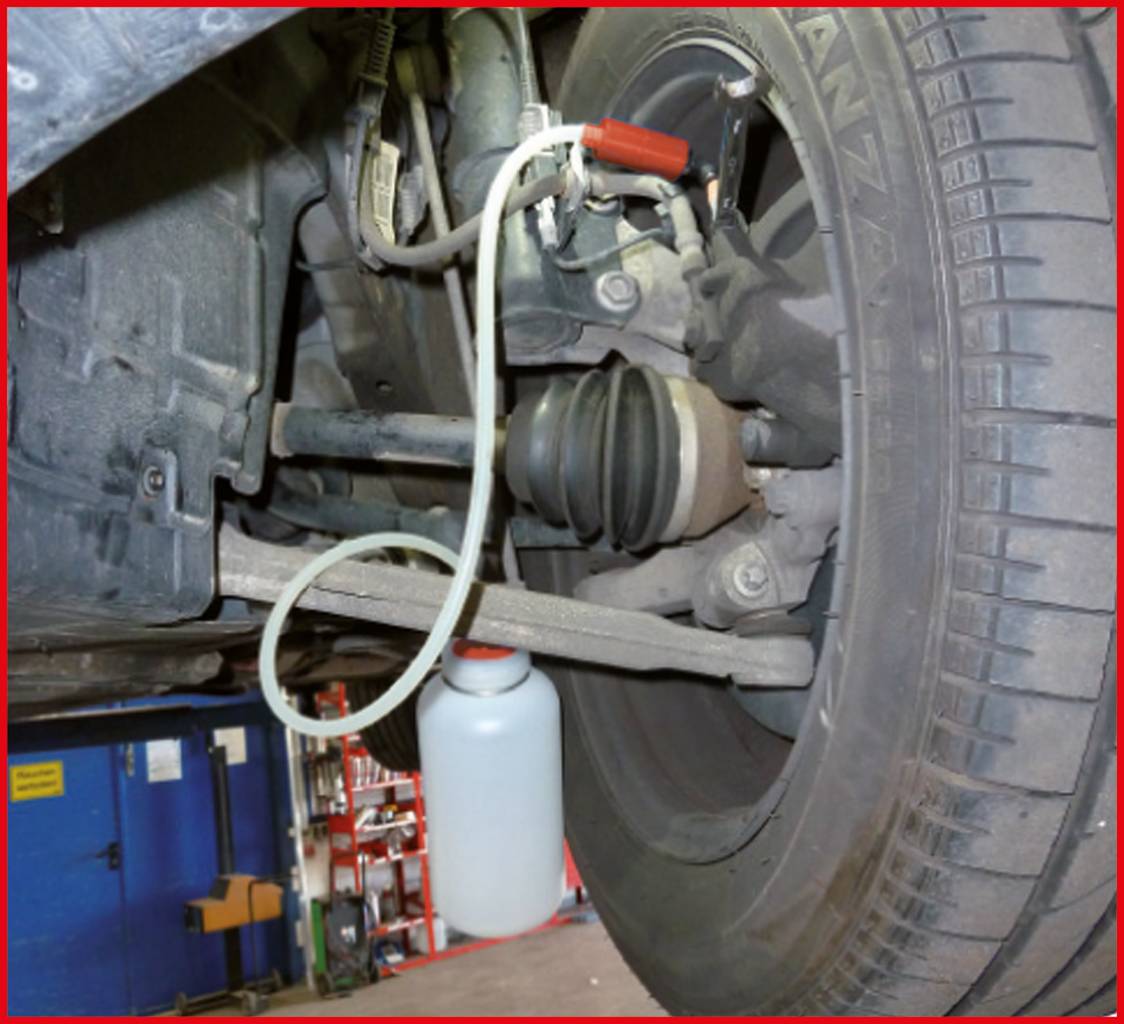 Ein Auto ist aufgebockt; eine Flasche hängt am Bremssattel, verbunden mit einem Schlauch, möglicherweise für Bremsflüssigkeitswechsel.