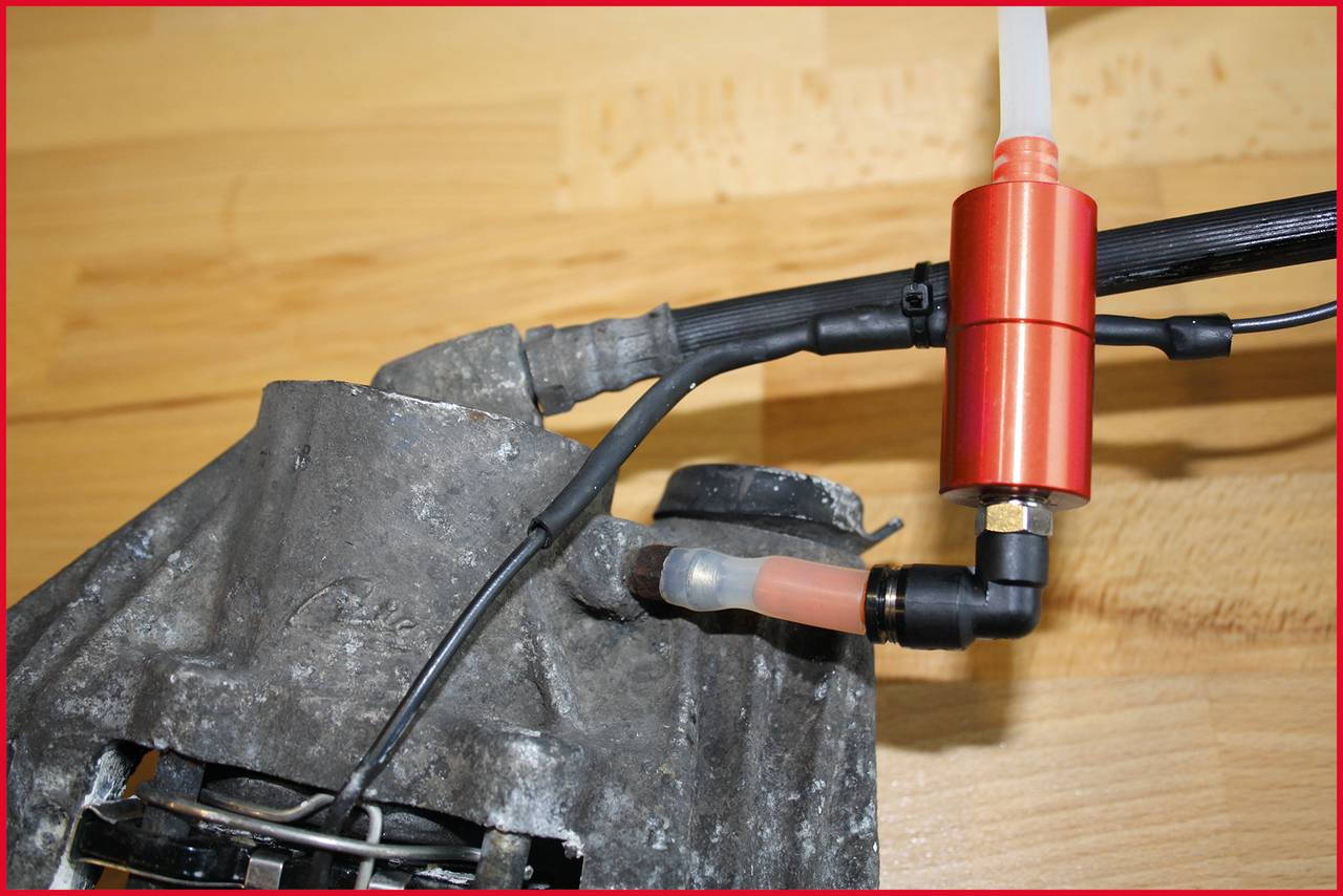 Ein Bremsentlüftersystem, bestehend aus einem roten Ventil und Schläuchen, an einer metallischen Autokomponente befestigt.