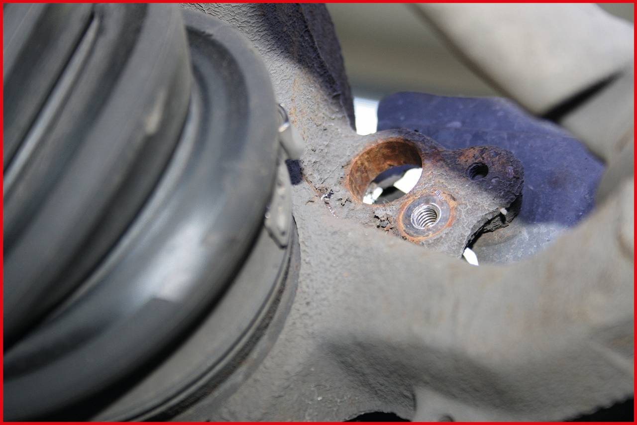 Nahaufnahme von einem rostigen Autoteil mit sichtbarer Schraube und Gummidichtung im Vordergrund; Detail eines Fahrzeugsystems.