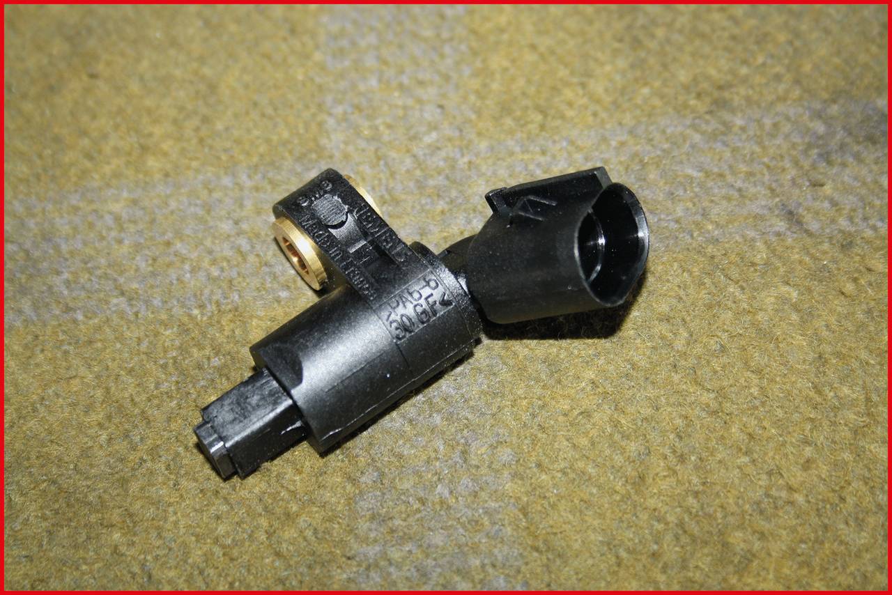 Ein schwarzer Sensor auf einem gelben Hintergrund. Der Sensor wirkt wie ein technisches Autoteil, möglicherweise ein Motorteil.