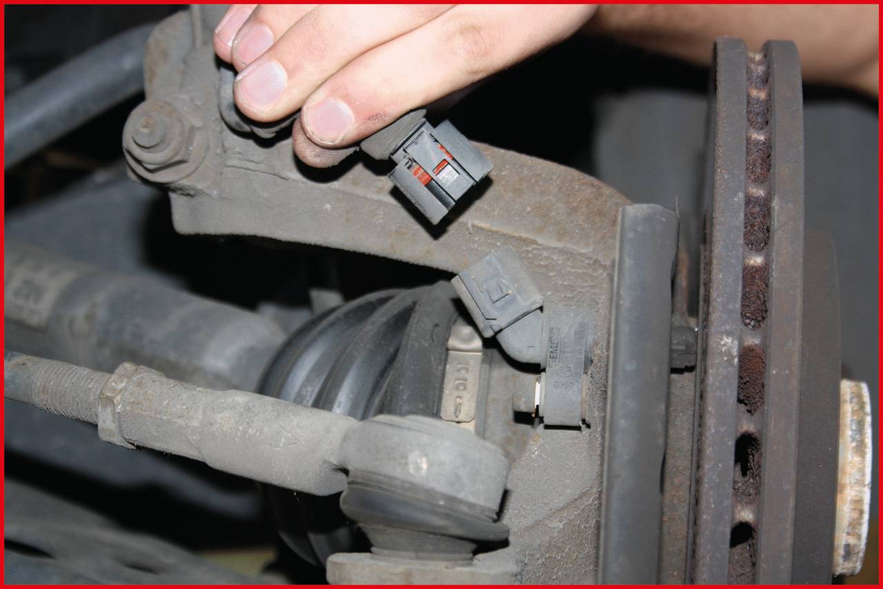Eine Hand hält einen elektrischen Steckverbinder in der Nähe von Automechanikteilen. Der Fokus liegt auf dem Stecker und den Teilen.