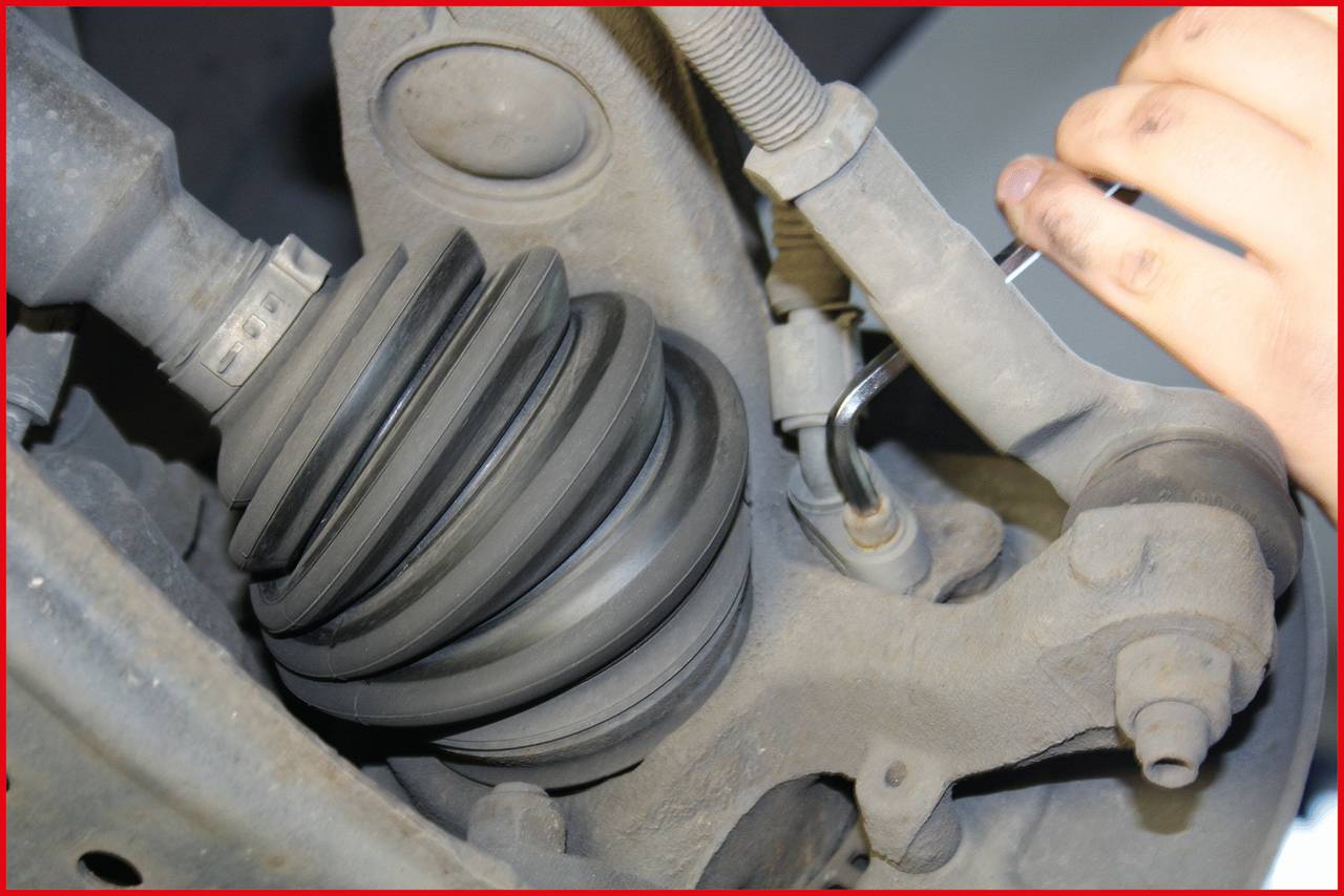 Ein Mechaniker justiert mit einem Werkzeug das Fahrwerk eines Fahrzeugs. Zu sehen ist ein Teil der Aufhängung mit Schraube und Dämpfung.