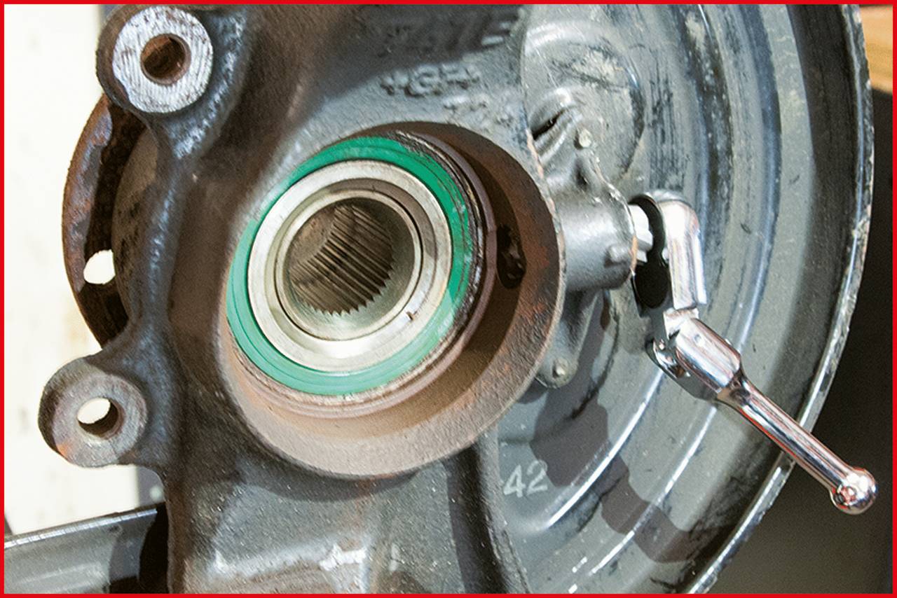 Die Nahaufnahme zeigt ein Metalllager in einem mechanischen Bauteil, umgeben von einem grünen Dichtungsring. Rechts daneben ein Metallwerkzeug.