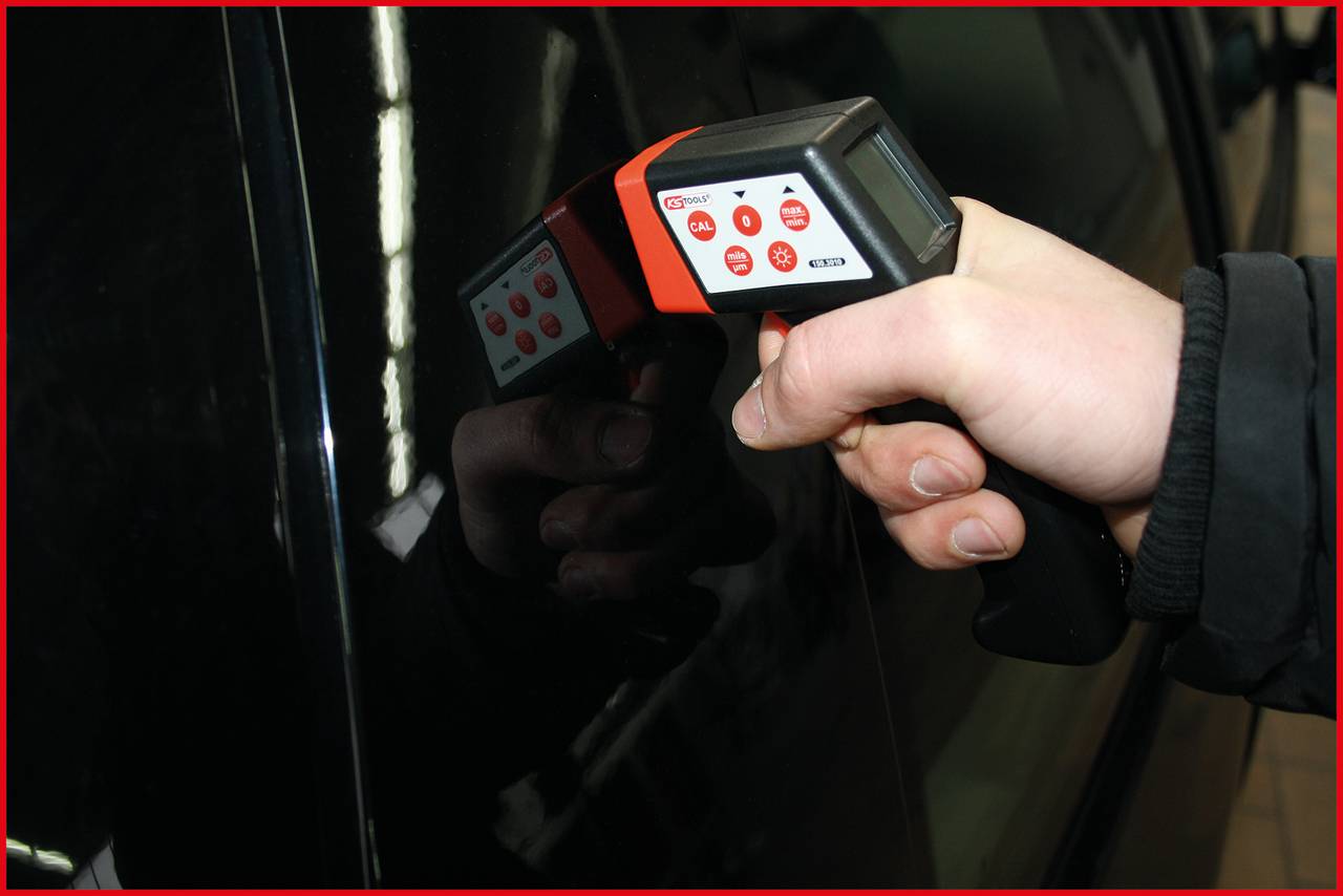 Eine Hand hält ein digitales Lackmessgerät an die Oberfläche eines schwarzen Autos, um die Dicke der Lackschicht zu überprüfen.