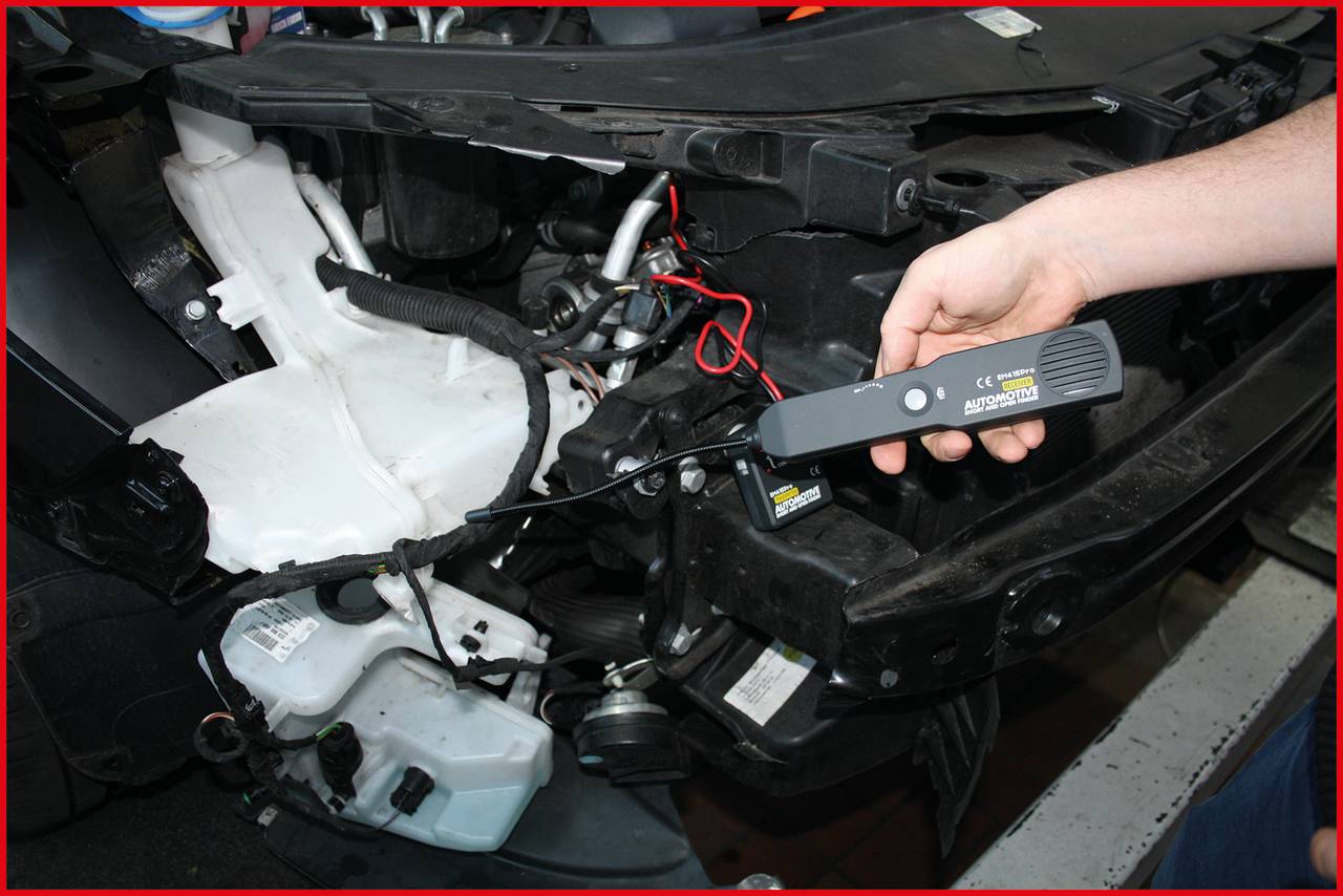 Eine Person testet die Verkabelung in einem Auto mit einem Diagnosegerät. Der Motorraum ist teilweise geöffnet.