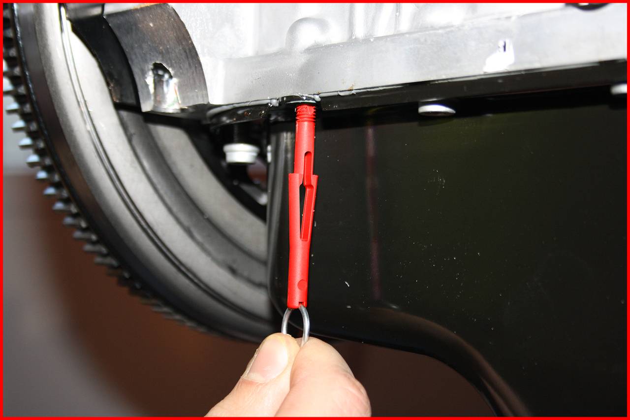 'Eine rote Kunststoffdübel wird von einer Hand gehalten und in ein Metallloch eingeführt.'