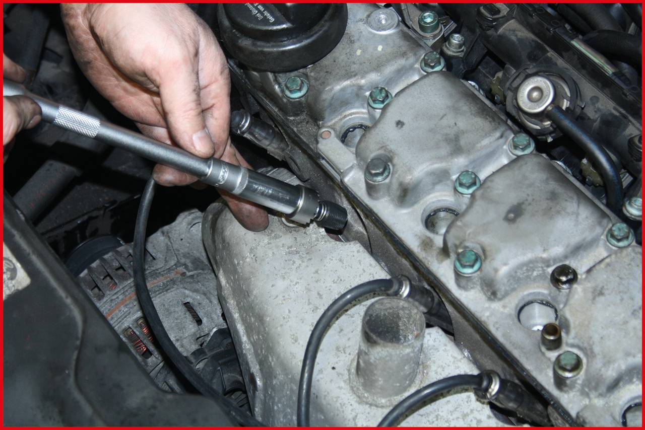 'Eine Person verwendet ein Werkzeug, um an einem Automotor zu arbeiten. Das Bild zeigt Details des Motorblocks und umgebende Komponenten.'