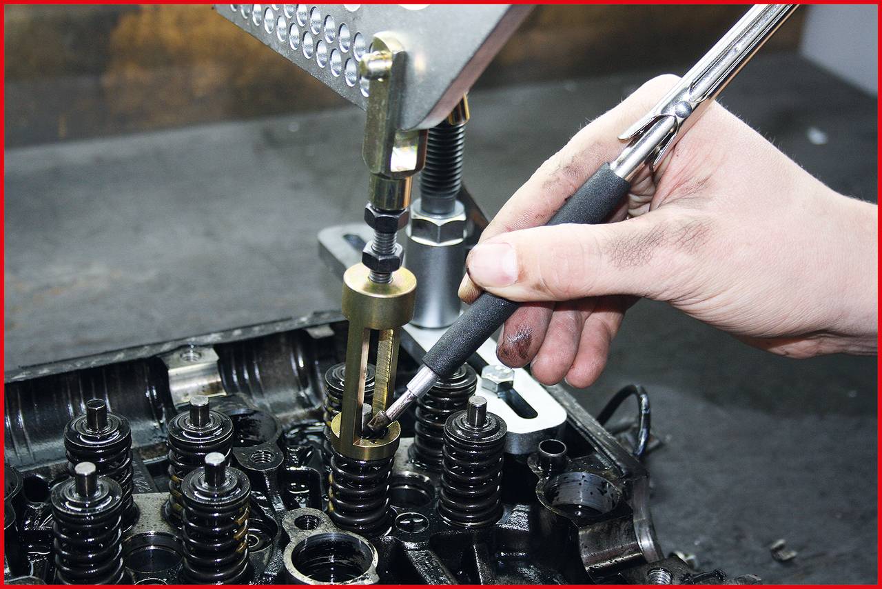 Eine Hand montiert eine Ventilfeder in einem Motor mit einem speziellen Werkzeug in einer Werkstattumgebung.